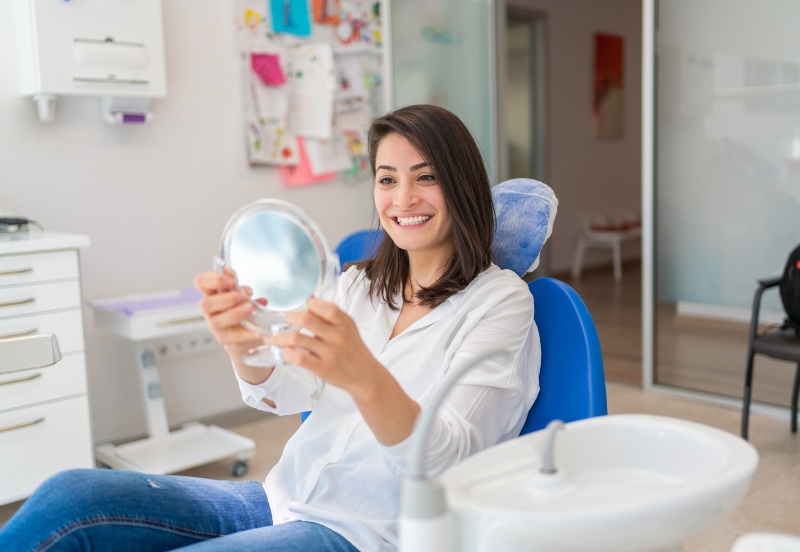 Woman looking at a mirror after getting full mouth dental implants in Kalamazoo, MI