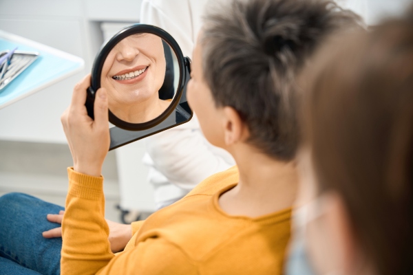 A woman gazes in the mirror, thinking about dental implants vs. dentures in Kalamazoo, MI.